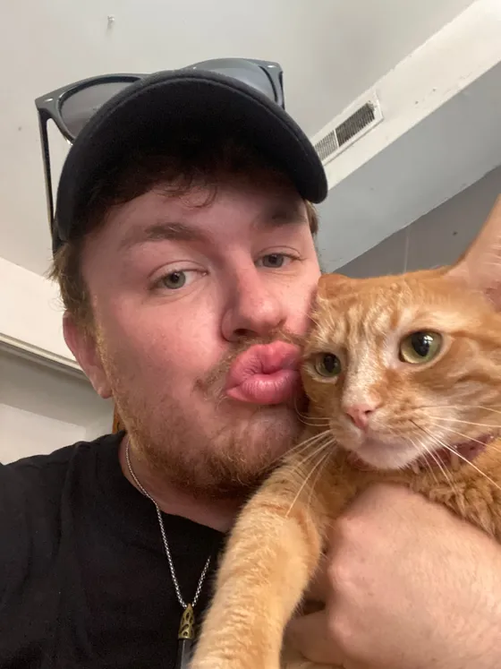 Edward kissing the head of Regina, an orange tabby cat draped over his arm